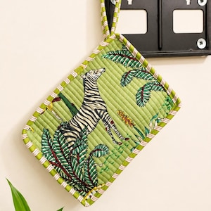 Puede incluir: Un agarrador de cocina acolchado rectangular con fondo verde claro y un patr&oacute;n estampado de una cebra y hojas de palmera tropicales. Los bordes est&aacute;n rematados con un ribete de tela a rayas verdes y blancas y una trabilla a juego para colgar.