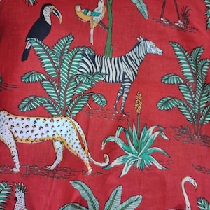 Puede incluir: Una tela roja con un patr&oacute;n repetitivo de varios animales y plantas. El dise&ntilde;o incluye un tuc&aacute;n negro, un p&aacute;jaro amarillo y azul, una cebra blanca y negra, un leopardo manchado y dos p&aacute;jaros blancos, intercalados con palmeras verdes.