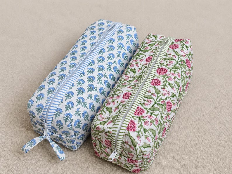 K&ouml;nnte beinhalten: Zwei rechteckige Federm&auml;ppchen. Eines ist wei&szlig; mit blauem Blumenmuster und blauem Streifenrei&szlig;verschluss. Das andere ist wei&szlig; mit rosa Blumenmuster und gr&uuml;nem Streifenrei&szlig;verschluss. Beide haben einen Rei&szlig;verschluss.