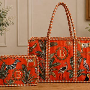 Puede incluir: Un bolso tote acolchado de color naranja y un estuche rectangular a juego, ambos con un estampado vibrante de temática selvática con animales, follaje tropical y una letra B bordada en el centro rodeada por una corona de laurel verde.