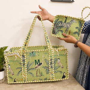 Puede incluir: Una cesta de almacenamiento rectangular acolchada y un agarrador cuadrado a juego en tela verde claro. Ambos art&iacute;culos presentan un estampado de selva con cebras, leopardos y aves. La cesta tiene una letra M bordada en verde en el panel frontal.