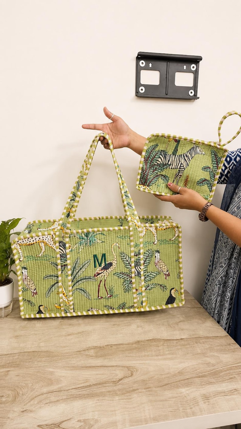 Puede incluir: Una cesta de almacenamiento rectangular acolchada y un agarrador cuadrado a juego en tela verde claro. Ambos art&iacute;culos presentan un estampado de selva con cebras, leopardos y aves. La cesta tiene una letra M bordada en verde en el panel frontal.