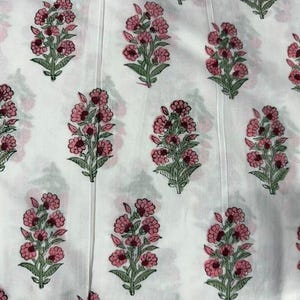 K&ouml;nnte beinhalten: Wei&szlig;er Stoff mit einem sich wiederholenden Muster aus rosa Blumenstr&auml;u&szlig;en mit gr&uuml;nen Bl&auml;ttern. Die Blumen haben eine dunkelrosa Mitte und einen hellrosa &auml;u&szlig;eren Rand. Der Stoff hat vertikale N&auml;hte.