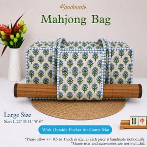 May include: A rectangular quilted Mahjong bag featuring a blue and green floral pattern on a cream background with blue and white striped trim. The bag includes an exterior pocket holding a rolled brown game mat. Dimensions are L 22" H 11" W 6".