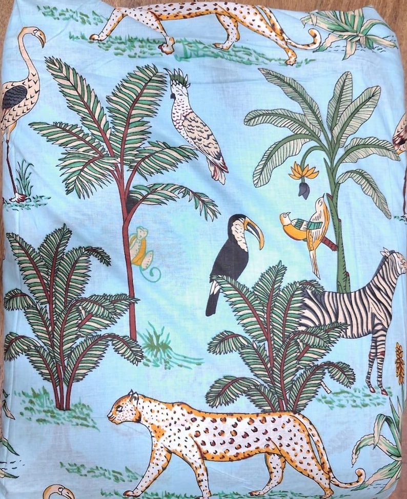 Puede incluir: Una tela azul claro con un patr&oacute;n repetitivo de animales de la selva y plantas tropicales. El estampado incluye un guepardo, una cebra, un tuc&aacute;n, una cacat&uacute;a y un flamenco, intercalados con palmeras y follaje en tonos verdes, amarillos y negros.