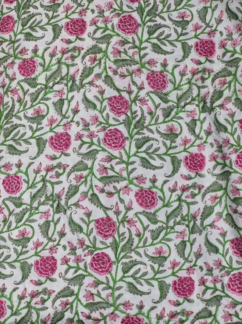 K&ouml;nnte beinhalten: Wei&szlig;er Stoff mit einem sich wiederholenden Blumenmuster. Das Design zeigt gro&szlig;e, leuchtend rosa pfingstrosenartige Bl&uuml;ten, kleinere rosa Knospen sowie gr&uuml;ne Bl&auml;tter und Stiele. Die Gesamt&auml;sthetik ist ein klassischer, botanischer Druck.