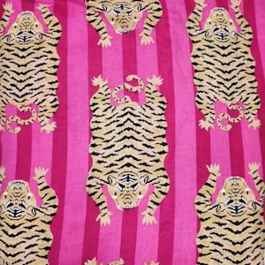 Puede incluir: Un tejido textil con un patr&oacute;n repetitivo de tigres de color tostado con rayas negras dispuestos en un dise&ntilde;o escalonado. El fondo consiste en rayas verticales alternas en dos tonos distintos de rosa brillante, creando un contraste audaz.