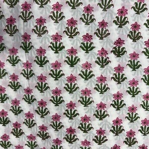 K&ouml;nnte beinhalten: Wei&szlig;er Stoff mit einem sich wiederholenden Muster aus rosa Bl&uuml;ten und gr&uuml;nen Bl&auml;ttern. Das florale Design ist gleichm&auml;&szlig;ig verteilt und erzeugt eine symmetrische Anordnung. Der Stoff ist wahrscheinlich Baumwolle oder ein &auml;hnliches Material.