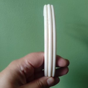 May include: A smooth, off-white bangle bracelet featuring a triple-layered design with three distinct, parallel rounded bands fused together into a single circular piece. The surface is solid and opaque with a consistent light cream color throughout.