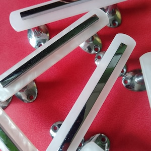 May include: A collection of rectangular cabinet pulls featuring a white, semi-translucent acrylic base with a centered, polished chrome metal inlay. Each handle includes two circular mounting bases with pre-drilled holes for installation.