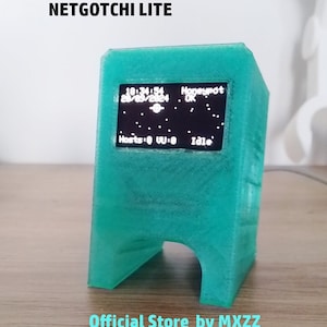 Może przedstawiać: Turkusowe urządzenie elektroniczne z napisem "NETGOTCHI LITE" u góry. Ekran wyświetla godzinę, datę i informacje o statusie. Na dole urządzenia znajduje się napis "Official Store by MXZZ".