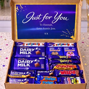 May include: A cardboard gift box filled with various Cadbury chocolate bars and treats. The inside lid features a blue sign with the text Just for You, To Hannah, Love Auntie Jess. X X. The box contains Dairy Milk, Curly Wurly, Twirl, and Wispa bars.