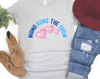 May include: A gray t-shirt with the text "Mama Runs The Show" in blue and pink lettering. There are three pink hearts with blue outlines above the text.
