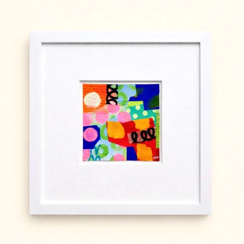 May include: Abstract art piece in a white frame. The artwork features a collage of colors, including pink, orange, blue, and green. The design incorporates circles, dots, and squiggly lines. The artwork is signed in the lower right corner.
