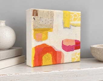 May include: A square canvas painting featuring an abstract collage design with textured layers of cream, bright yellow, vibrant orange, and pink paint. The composition includes torn paper elements, speckled ink details, and white line drawings on a textured surface.