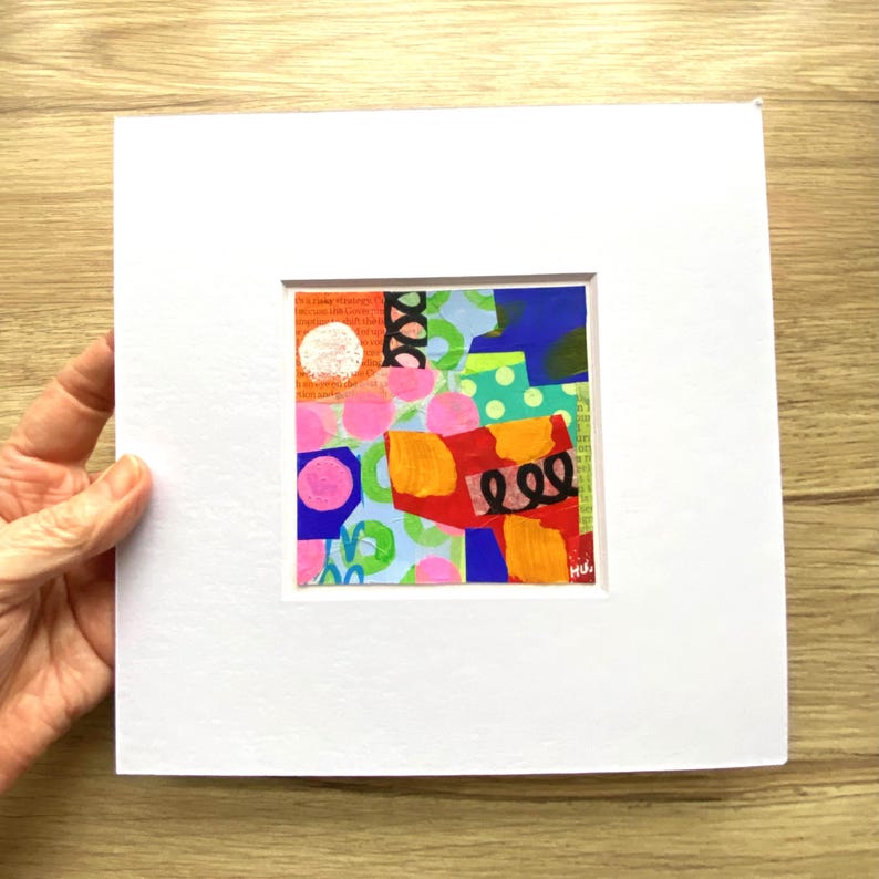 May include: Abstract art piece with a white mat. The artwork features a collage of colorful shapes, including pink circles, orange brushstrokes, and blue and green geometric forms. The piece is signed in the lower right corner.