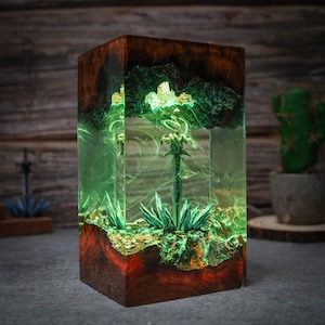 Puede incluir: Una espada verde brillante encapsulada en resina transparente con una base de madera. La espada est&aacute; rodeada de follaje verde y la resina tiene un efecto de remolino.