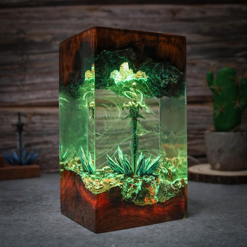 Puede incluir: Una espada verde brillante encapsulada en resina transparente con una base de madera. La espada est&aacute; rodeada de follaje verde y la resina tiene un efecto de remolino.