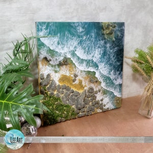 Pode incluir: Um close-up de uma obra de arte em resina que retrata uma costa rochosa com ondas quebrando. As ondas s&atilde;o brancas e azuis, e as rochas s&atilde;o cinzas e marrons. H&aacute; um pequeno peda&ccedil;o de musgo verde nas rochas.