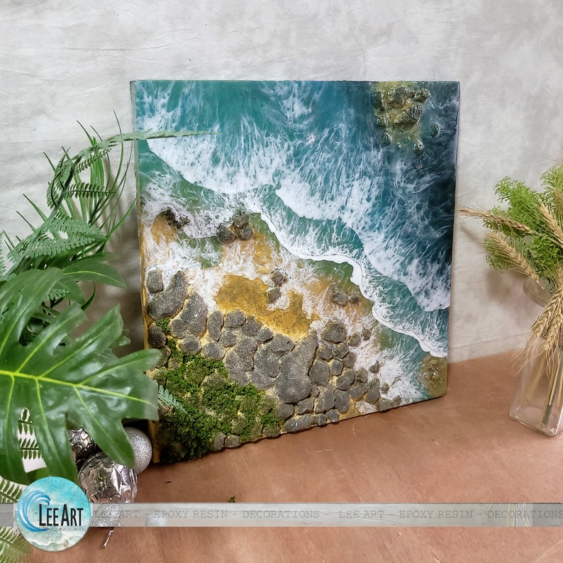 Pode incluir: Um close-up de uma obra de arte em resina que retrata uma costa rochosa com ondas quebrando. As ondas s&atilde;o brancas e azuis, e as rochas s&atilde;o cinzas e marrons. H&aacute; um pequeno peda&ccedil;o de musgo verde nas rochas.