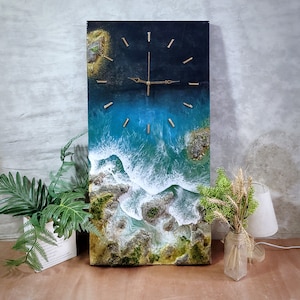 May include: A rectangular wall clock with a coastal design. The clock face depicts a detailed ocean scene with blue and white waves, rocky shores, and gold-colored clock hands and markers. The clock is a decorative piece for home decor.