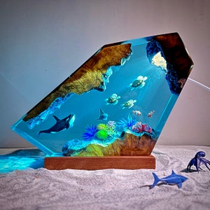 May include: A resin sculpture of an ocean scene with a whale, sea turtles, and coral. The sculpture is mounted on a wooden base and has a blue, green, and brown color scheme.