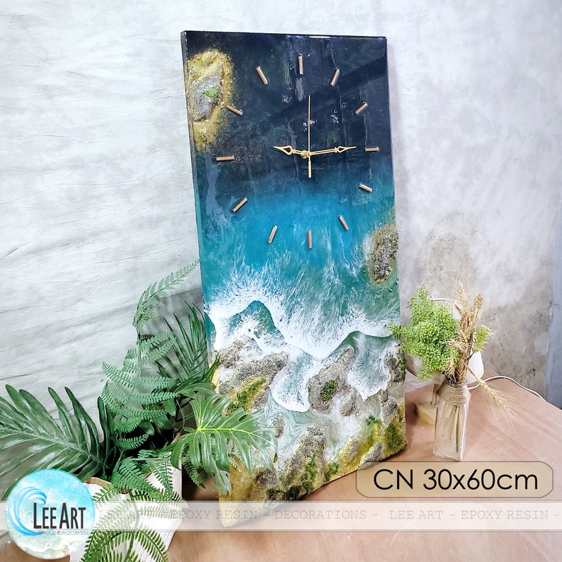K&ouml;nnte beinhalten: Eine rechteckige Wanduhr mit einem Harz-Ozean-Design. Das Zifferblatt zeigt eine blau-wei&szlig;e Ozeanszene mit goldfarbenen Zeigern und Markierungen. Die Uhr misst 30 x 60 cm und tr&auml;gt den Text "CN 30x60cm".