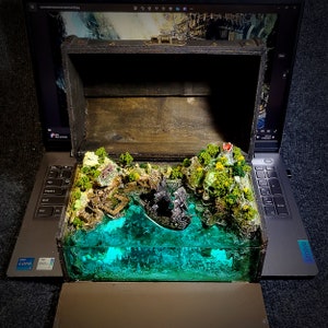 May include: A wooden treasure chest with a green and brown diorama inside. The diorama depicts a sunken ship with a green, blue, and white water effect.