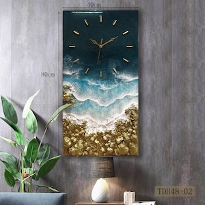 K&ouml;nnte beinhalten: Eine Wanduhr aus Harz mit einem Design aus blauen und goldenen Ozeanwellen. Die Uhr ist 40 cm breit und 80 cm hoch. Das Zifferblatt der Uhr ist schwarz mit goldenen Zeigern und goldenen Stundenmarkierungen.
