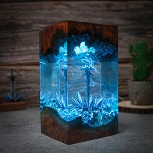 Puede incluir: Un bloque de resina azul con dos espadas plateadas incrustadas. El bloque est&aacute; iluminado desde el interior, creando un efecto brillante. El bloque est&aacute; sentado sobre una base de madera.