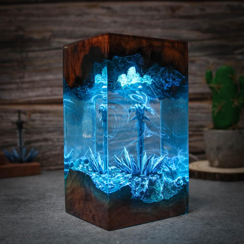 Puede incluir: Un bloque de resina azul con dos espadas plateadas incrustadas. El bloque est&aacute; iluminado desde el interior, creando un efecto brillante. El bloque est&aacute; sentado sobre una base de madera.