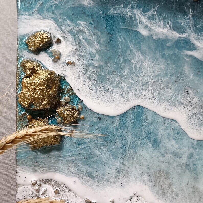 K&ouml;nnte beinhalten: Nahaufnahme eines Harz-Kunstwerks, das einen blauen Ozean mit wei&szlig;en Wellen darstellt, die an einem Ufer mit goldenen Akzenten brechen.