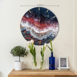 Puede incluir: Un reloj de pared redondo de resina con un diseño abstracto en negro, rojo, blanco y dorado. El reloj tiene un diámetro de 40 cm y tiene agujas y números dorados.