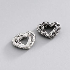 May include: Two heart-shaped stud earrings, each featuring a double-heart design with a textured, hammered metal surface. One earring is finished in a bright silver tone, while the other has a darkened, oxidised silver finish.