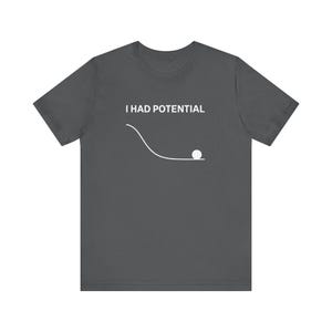 May include: Dark grey t-shirt with the text "I HAD POTENTIAL" above a white graphic of a ball rolling down a curved path. The shirt is a short-sleeved crew neck.
