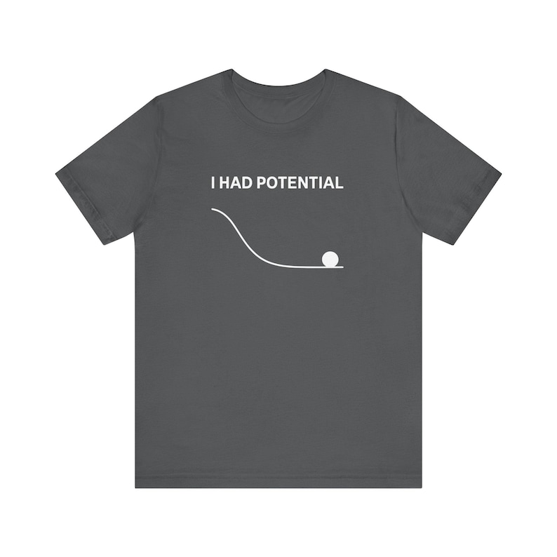 May include: Dark grey t-shirt with the text "I HAD POTENTIAL" above a white graphic of a ball rolling down a curved path. The shirt is a short-sleeved crew neck.
