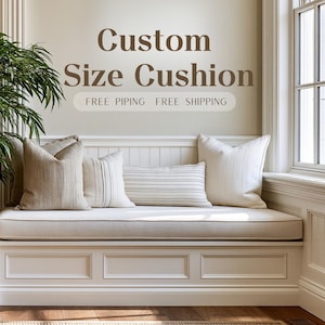 Puede incluir: Un cojín a medida sobre un banco blanco con varios cojines decorativos. El texto Custom Size Cushion aparece sobre el banco, con el texto FREE PIPING FREE SHIPPING debajo. Los cojines son de tonos neutros beige y blanco.