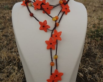 May include: A long orange and brown beaded necklace with orange flower-shaped beads. The necklace is displayed on a white mannequin.
