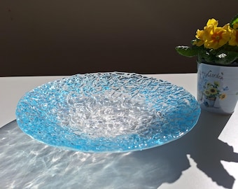 Könnte beinhalten: Eine klare Glasschüssel mit einer strukturierten Oberfläche und einem hellblauen Rand. Die Schüssel steht auf einer weißen Oberfläche.