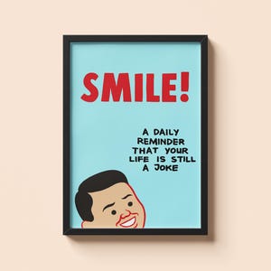 May include: Framed art print with a light blue background and the word "SMILE!" in red. The print includes the text "A daily reminder that your life is still a joke" and a cartoon face.