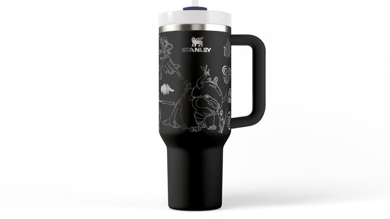 May include: Black Stanley tumbler with a white lid, handle, and straw. The tumbler features a detailed white graphic design of various characters and the Stanley logo. The tumbler is designed to keep beverages cold or hot.