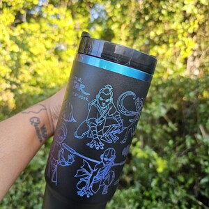 May include: Black tumbler with a blue and purple illustration of characters from Avatar: The Last Airbender. The tumbler has a black lid and a blue accent band. The text "Avatar The Last Airbender" is visible on the side.