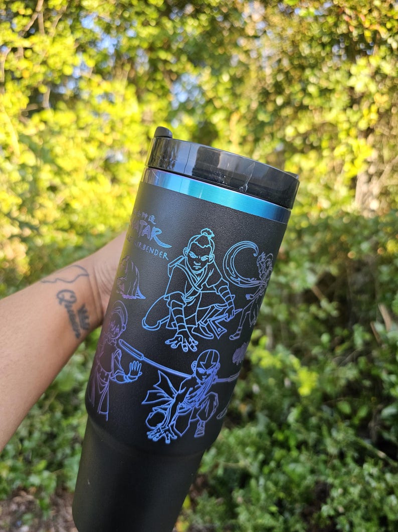 May include: Black tumbler with a blue and purple illustration of characters from Avatar: The Last Airbender. The tumbler has a black lid and a blue accent band. The text "Avatar The Last Airbender" is visible on the side.