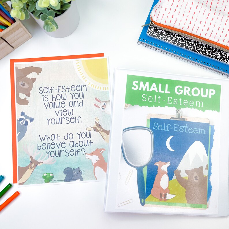 May include: A white binder with a green and white label that says "Small Group Self-Esteem". The binder has a clear pocket on the front that contains a worksheet with a cartoon fox and bear. The worksheet has the text "Self-Esteem" on it.