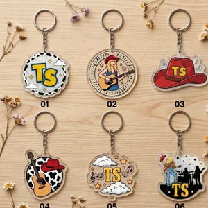 May include: Six acrylic keychains with metal rings. 01: circular with cow print and yellow TS. 02: circular with a person playing guitar. 03: red cowboy hat with yellow TS. 04: circular with cow print, guitar, and red hat. 05: clouds, stars, and yellow TS. 06: silhouette of a band with yellow TS.