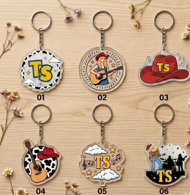 May include: Six acrylic keychains with metal rings. 01: circular with cow print and yellow TS. 02: circular with a person playing guitar. 03: red cowboy hat with yellow TS. 04: circular with cow print, guitar, and red hat. 05: clouds, stars, and yellow TS. 06: silhouette of a band with yellow TS.