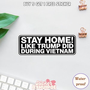May include: A white sticker with black text that reads "STAY HOME! LIKE TRUMP DID DURING VIETNAM." The sticker has a black border and is on a white surface. The text "BUY 5 GET 1 FREE STICKER" is at the top.
