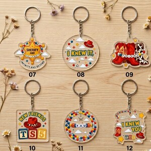 May include: Six clear acrylic keychains featuring colorful designs inspired by western themes. Designs include a sheriff badge, cowboy hats, boots, and lettered beads. Each keychain has a metal ring and chain, labeled with numbers 07 through 12.