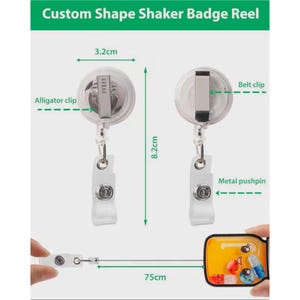 Puede incluir: Un carrete de insignia agitador de forma personalizada transparente con un clip de cocodrilo y un pasador met&aacute;lico. El carrete mide 3,2 cm de ancho y 8,2 cm de largo, con un cable retr&aacute;ctil de 75 cm. El texto "Custom Shape Shaker Badge Reel" est&aacute; en la parte superior.