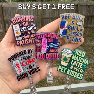 Puede incluir: Una colecci&oacute;n de carretes de insignia brillantes con varios dise&ntilde;os y texto. Los carretes presentan frases como "Running on Celsius", "Powered by Diet Coke" y "Iced Matcha Latte & Pet Kisses". Cada carrete tiene un esquema de color diferente e incluye im&aacute;genes de bebidas.